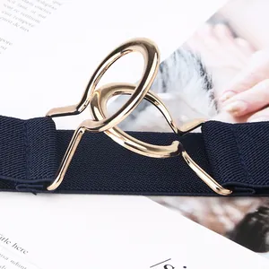 Women's black elastic waist belt with gold interlocking metal buckle on a fashion magazine