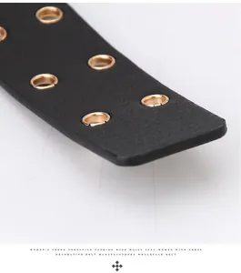 Detail of black leather belt with double row of gold grommets and litchi texture