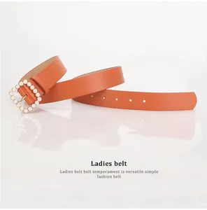 Detail of orange-brown leather belt with square gold buckle and faux pearl accents