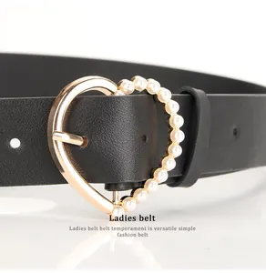 Detail of heart-shaped gold buckle with inlaid white pearls on a black leather belt