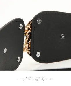Detail of vintage gold buckle with embossed texture on black elastic waist belt