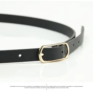 Détail d'une ceinture fine en similicuir noir avec une boucle rectangulaire dorée polie