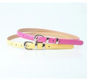 Detail of skinny patent leather belts in pink and yellow with silver metal buckles