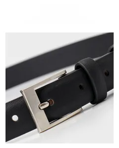Détail d'une ceinture en cuir noir avec boucle en alliage brossé sur un fond blanc épuré