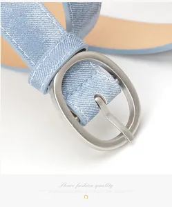 Detail of light blue denim texture belt with a matte silver oval buckle and fine stitching