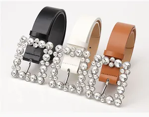 Three leather belts in black white and brown featuring large rhinestone square buckles