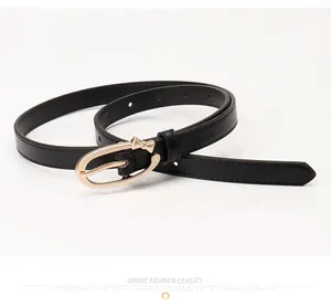 Detail of slim black PU leather belt featuring a gold oval buckle with bow decoration