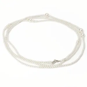 Elegant long white pearl necklace and waist chain with silver lobster clasp on white surface