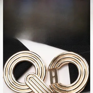 Detailed close-up of a textured gold round metal buckle on a black elastic waist belt