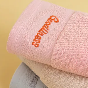 Thick pink cotton towel with Goodness embroidery stacked on neutral face towels