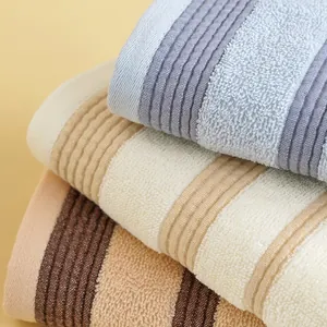Trois serviettes en coton rayées en bleu, blanc et beige avec des textures douces