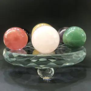 Nahaufnahme bunter Naturkristallkugeln auf facettiertem Glassockel mit tiefen Reflexionen