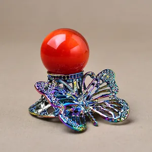 Dettaglio del supporto a farfalla arcobaleno con sfera di pietra arancione e strass