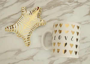 Close-up of ceramic jewelry tray with gold zebra patterns and a love heart coffee mug