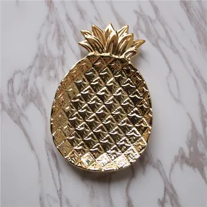Golden pineapple ceramic jewelry tray with textured surface on marble background