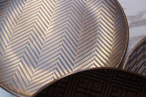Close-up of golden ceramic plate with embossed wave patterns and metallic finish