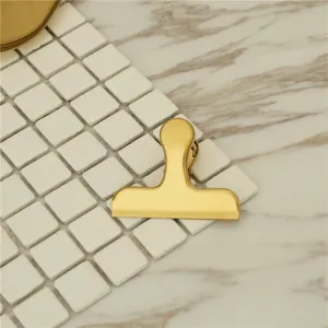 Minimalist gold stainless steel binder clip on a white tile and marble background