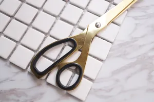 Nordic gold stainless steel scissors with black rubber grips on marble background