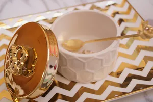 White ceramic honey jar with golden bee lid, honeycomb texture and small spoon