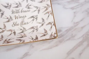 Detail of ceramic jewelry tray featuring gold rim and brave wings bird print