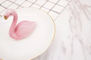 Plateau à bijoux flamant en céramique avec bord doré sur fond en marbre, vue latérale