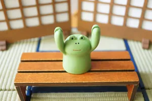 Cute green frog figurine holding hands up as a desk card holder on a wooden bench