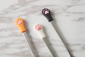 Cute stainless steel cat paw coffee spoons with 3D pink pads on marble surface