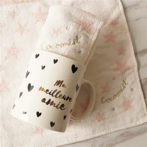 Détail d'un mug en céramique avec broderie dorée sur une serviette rose texturée