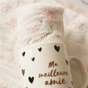 Détail d'une serviette en coton avec étoiles roses et broderie dorée dans un mug