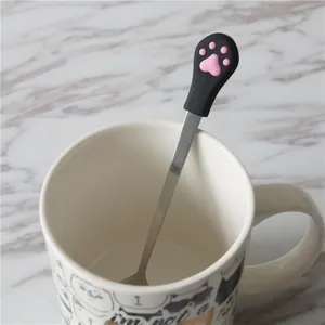 Close-up of a stainless steel cat paw coffee spoon in a white ceramic mug on marble