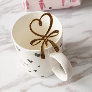 Détail d'une cuillère à café dorée cœur et nœud sur un mug en céramique blanche