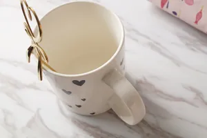 Élégante tasse en céramique blanche avec cœur et cuillère dorée sur marbre