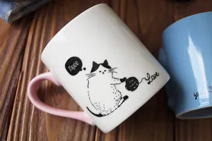 Detail of ceramic cat mugs with hand-painted illustrations and pink heart handles