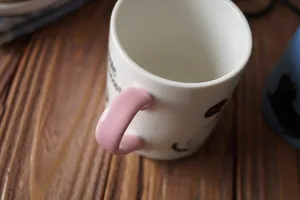 Detail of pink handle and cat pattern on a white ceramic mug on a wooden table