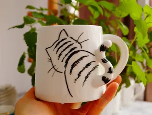 Primer plano de una taza de cerámica blanca con diseño de gato y asa en forma de cola