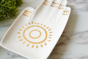 Witte keramische sieraden schotel in handvorm met gouden zon op marmeren basis