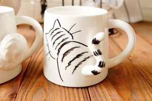 Primer plano de una taza de cerámica blanca con asa en forma de cola de gato y dibujo