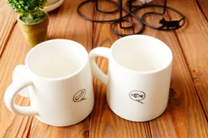 Detalle de tazas de cerámica blanca con dibujos de huesos y peces sobre mesa de madera