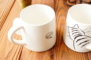 Primer plano detallado de una taza de cerámica blanca con dibujos de gatos y huesos sobre madera