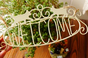 Vintage metal welcome sign with cat silhouettes and scrolls on a rustic hanging rope
