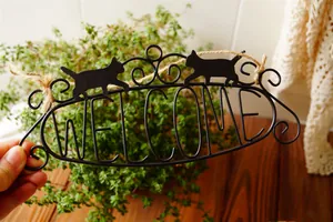 Close-up of vintage black metal Welcome sign with cute cat silhouettes and rustic twine