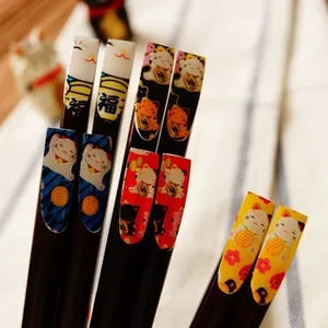 Lot de baguettes japonaises en bois naturel avec motifs Maneki-neko colorés sur nappe rayée