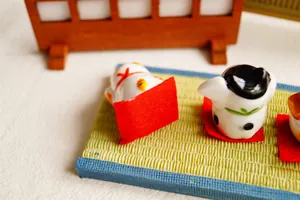 Three mini ceramic fortune cat figurines on tatami mat with wooden screen background