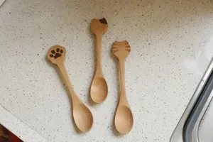 Vue détaillée de trois cuillères en bois avec manches sculptés en forme de patte et tête de chat