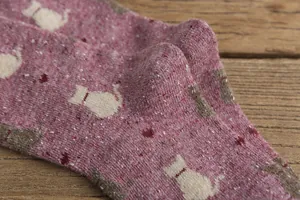 Macro detail of retro pink knitted crew socks featuring cute cat patterns and marled texture