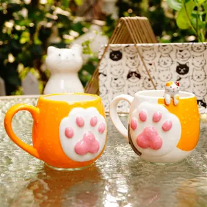 Detailed view of two ceramic cat paw mugs with 3D feline figures in a sunny garden setting