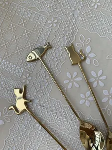 Detailed view of three gold stainless steel spoons with cat and fish handle designs