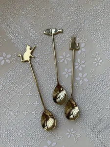 Detailed close-up of three golden cat and fish handle spoons on a lace tablecloth