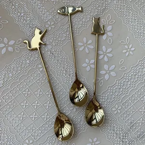 Three-piece gold cat and fish stainless steel coffee spoons on elegant lace fabric