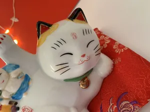 Close-up of ceramic Maneki Neko figurine with Kaiun text on a red embroidered cushion